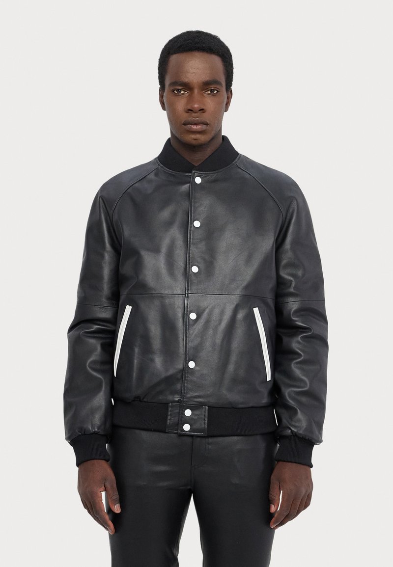 Black leather bomber jacket with raglan sleeves, snap buttons, white accents on pockets, and ribbed cuffs and waistband.