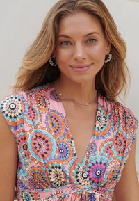 Colorful patterned dress featuring geometric designs in pink, orange, and blue, with a V-neckline and short sleeves. Silver accessories included.