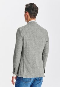 Szary blazer w jodełkę z klapami, usztywnionymi ramionami i bocznymi wentylami, zestawiony z dżinsami.