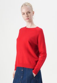 Red knitted sweater with a crew neckline, ribbed cuffs and hem, soft texture, and relaxed fit, paired with a denim skirt.