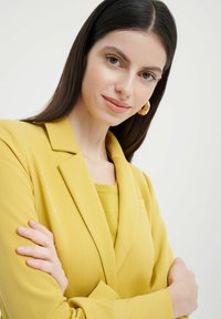 Blazer giallo dal design sartoriale con rever a punta, abbinato a un top giallo coordinato. Tessuto morbido, maniche lunghe e vestibilità comoda.