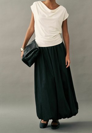 Weißer drapierter Oberteil kombiniert mit einem schwarzen, voluminösen Rock. Verfügt über ein lässiges Design und eine strukturierte schwarze Clutch. Ergänzt mit flachen schwarzen Schuhen.