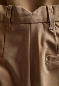 Bruine broek met een gladde textuur, zichtbare stiksels en een recht model. De tailleband heeft plooien en een riemlus.