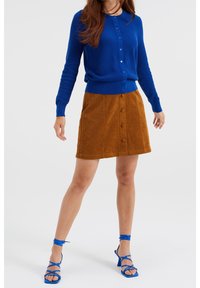 Blå stickad kofta med rund halsringning, tillsammans med en brun kordflor A-linjeformad kjol med knapprad och blå remsandaler.