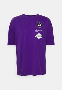 Camiseta de algodón morada con mangas cortas. Presenta logotipos: "LA", el swoosh de Nike y un gráfico de baloncesto de "Los Angeles Lakers" en colores contrastantes.