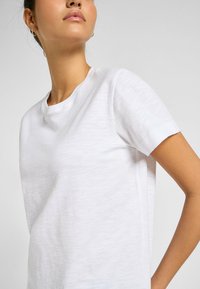 T-shirt bianca a girocollo realizzata in un tessuto leggero e testurizzato. Maniche corte, vestibilità rilassata, con design minimalista, senza motivi visibili o accessori.