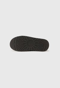 Semelle de chaussure en caoutchouc noir avec surface texturée présentant un motif en étoile et des accents surélevés pour une meilleure traction. Bout arrondi pour plus de confort.
