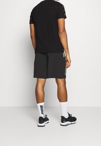 Camiseta negra de manga corta, combinada con pantalones cortos negros. Los detalles notables incluyen acentos de logo y calcetines blancos de caña corta con zapatillas negras.