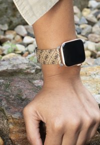 Ceas inteligent cu cadran dreptunghiular negru, accesorii aurii și o curea bej cu design modelat și detalii cusute.