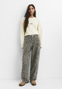 Svetlo rumena oversize dukserica s "STWD" logotipom, u kombinaciji s širokim leopard print hlačama i smeškim cipelama na slip-on.