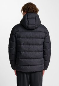 Zwarte gewatteerde jas met een hoge kraag, doorgestikt patroon en een afneembare capuchon. De stof lijkt glad en glanzend, en biedt isolatie.