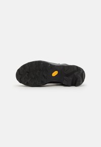 Čierna gumová podrážka s výraznými dezénmi; obsahuje žlté logo Vibram; aerodynamický dizajn s vystuženými okrajmi.
