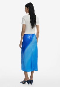 Blauwe pailletten midi rok met een gradiëntontwerp, gladde textuur, een split aan de achterkant, gecombineerd met een crème aansluitend T-shirt en blauwe hakken.
