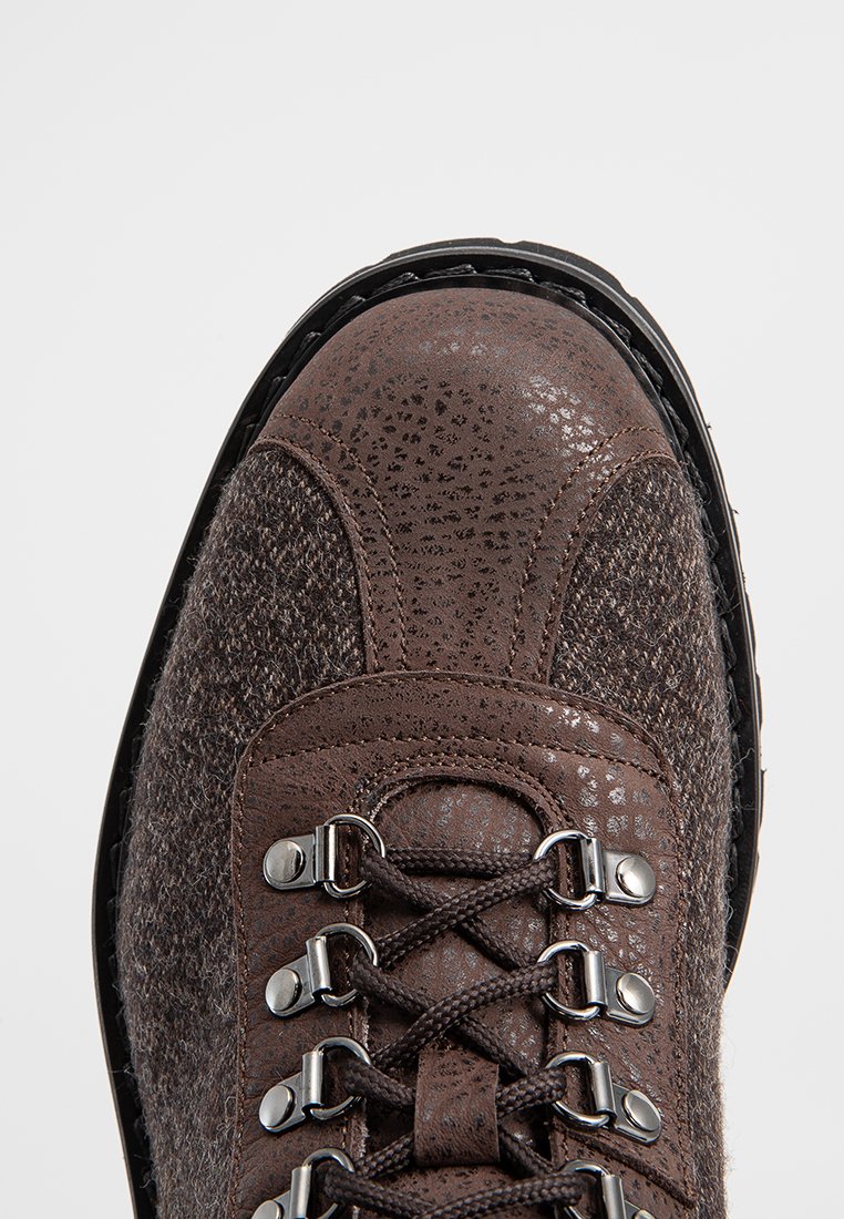 Botte de randonnée marron avec une tige en cuir texturé et un embout en cuir lisse,œillets en métal et lacets. Semelle en caoutchouc noir crantée.