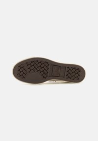 Brown rubber shoe sole with a textured herringbone pattern and a rectangular logo label. Smooth beige side edge.