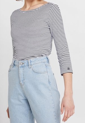 Czarnobiały paskowany top z długim rękawem i okrągłym dekoltem, zestawiony z jasnoniebieskimi, wysokim stanem jeansami zapinanymi na guzik.