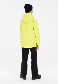Veste imperméable jaune vif avec capuche, associée à un pantalon noir et des bottes noires robustes. Design simple, adapté aux activités de plein air.