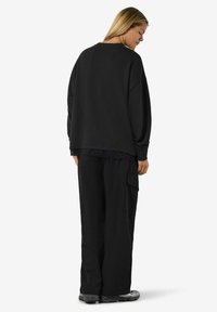 Felpa nera oversize con spalle scese, abbinata a pantaloni cargo neri. Tessuto morbido con un dettaglio in pizzo testurizzato visibile all'orlo.