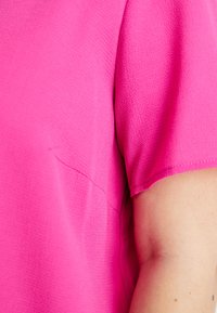 Blusa fúcsia com um tecido de textura suave, mangas curtas e um discreto detalhe de costura. Corte contemporâneo com um ajuste relaxado.