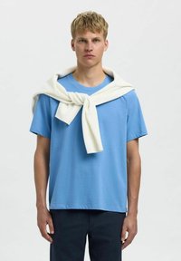 Gai zils īsās piedurknēm T-krekls, kas apvienots ar balto džemperi, kas uzmest svērumu uz pleciem. Vienkārša dizaina; gluda tekstūra. Tumšas bikses.