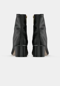 Une paire de bottines en cuir noir avec des talons blocs et des fermetures éclair dorées sur le côté, vues de l'arrière sur un fond blanc.
