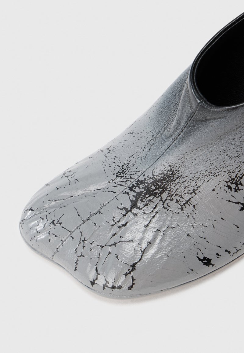 Gros plan sur une chaussure en cuir grise à bout carré avec un motif noir craquelé et une texture lisse et brillante.