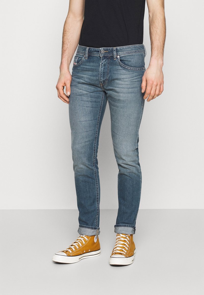 Blå denimjeans med slim fit och urtvättad effekt, ihopparade med bruna hög-top sneakers med vita snören och gummisula.