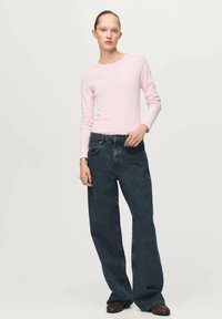 Svetlo roza dolg rokav majica s okroglim ovratnikom, v kombinaciji z ohlapnimi temno modrimi kavbojkami. Minimalističen dizajn, gladka tekstura.
