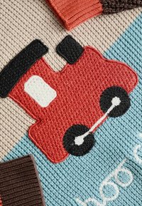 Voiture jouet rouge tricotée avec des roues noires et une fenêtre blanche sur un fond tricoté texturé bleu et beige.