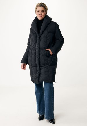 Zwarte pufferjas met een hoge kraag, gequilt ontwerp, zijzakken en een relaxte pasvorm, gecombineerd met blauwe flared jeans en zwarte schoenen.