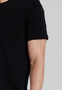 Black short-sleeve t-shirt made of soft cotton, featuring a round neckline and a small logo on the chest, smooth texture, fitted design.
