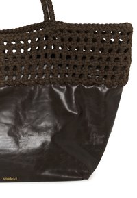 Sac fourre-tout marron foncé avec une partie supérieure tissée et des poignées tressées, corps inférieur lisse, et petit logo doré « soaked » dans le coin inférieur.