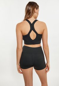 Schwarzer Sport-BH mit Kreuzträgerdesign und offenem Rückendetail, kombiniert mit schwarzen hoch geschnittenen Shorts, beide aus einem glatten, dehnbaren Material.