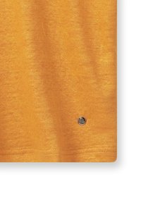 Camiseta de algodón amarilla con una textura suave, que presenta un pequeño acento de logo metálico y un diseño simple y sin costuras.