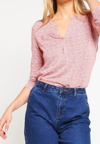Langærmet, pink mønsteret bluse med en nappeudskæring, parret med høj talje, mørkeblå denim jeans med knaplukning og lommer.