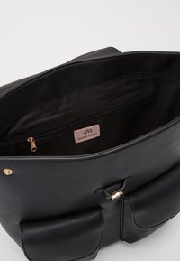 Sac à main en cuir noir avec une finition texturée, poche intérieure et quincaillerie dorée. Comprend un rabat avec une fermeture magnétique et un logo.