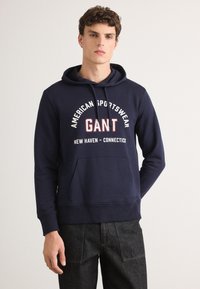Granatowy hoodie wykonany z bawełny, z przednią kieszenią kangurką, regulowanym sznurkiem i graficznym logo z tekstem na klatce piersiowej.