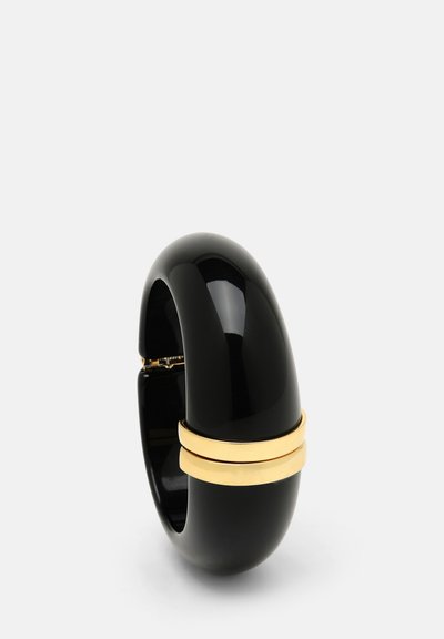 Czarna plastikowa bransoletka w kształcie bangla o gładkim, błyszczącym wykończeniu i złotej metalowej wstawce wokół środka. Zaokrąglony, konturowany kształt.