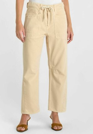 Pantalon beige à jambes larges avec grandes poches plaquées à l'avant et taille à cordon, porté avec des sandales à talons ouvertes marron.