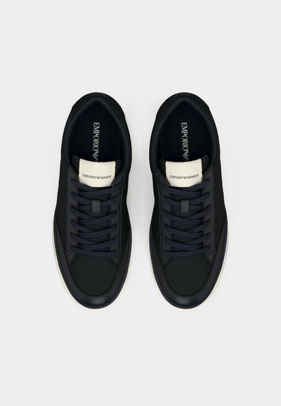 Črni supergi z gladkim tkaninskim zgornjim delom, mornarsko modrimi vezalkami in belim poudarkom okoli ovratnika. Gumijast podplat z minimalnim vzorcem tekalne plasti.