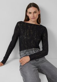 Schwarzes, langärmeliges, strukturiertes Strickoberteil mit weitem Ausschnitt, kombiniert mit hochtaillierten, grauen Jeans.