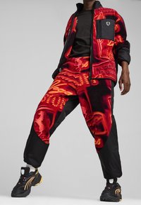 Red and black fleece tracksuit with neon graphic patterns, featuring a zip jacket and pullover design; paired with black sneakers.