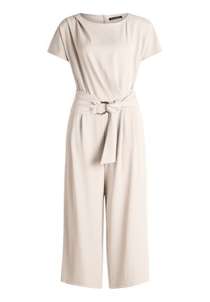 Combinaison beige à manches courtes avec jambes larges, encolure ronde et ceinture assortie en tissu avec boucle métallique circulaire à la taille.