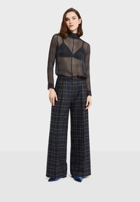 Průhledný černý kostkovaný top s dlouhými rukávy v kombinaci s širokými kostkovanými kalhotami navy barvy s kostkovaným vzorem a modrými podpatky.