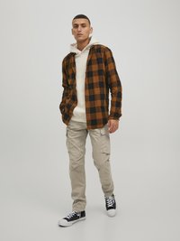 Brown and black checkered flannel shirt over a white hoodie, paired with beige cargo pants and black and white sneakers. Casual design.