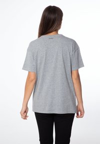 Camiseta de algodón gris con mangas cortas y un corte relajado, con un cuello redondo y el logo "protesta" cerca del cuello de la parte posterior.