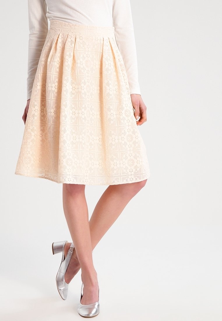 Vaalean persikan sävyinen pitsihame, jossa on A-linjainen siluetti, hienostuneita kukkakuvioita, laskoksia vyötäröllä ja sileä pinta. Hopeiset korot täydentävät asua.