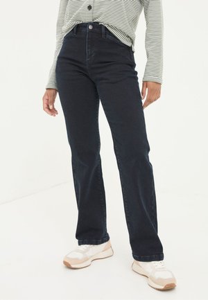 Person wearing high-waisted dark blue jeans, striped long-sleeve shirt, and white sneakers, standing against a plain white background.