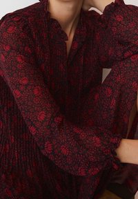 Pitkähihainen, tummasta kankaasta valmistettu mekko, jossa on punainen kukkakuosi, ry gathered kaula-aukko ja röyhelömäiset hihat, esittäen tekstuuri- ja kerroksellista ilmettä.