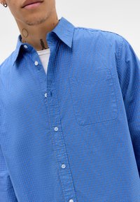 Blue checkered button-up shirt made of woven fabric, featuring a classic collar and a single chest pocket.